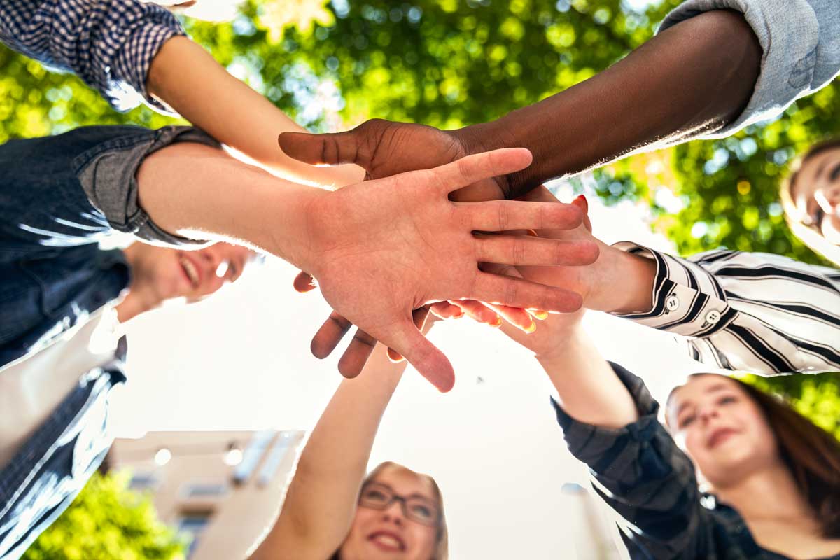 people in community standing in circle with outstretched arms and hands on top of one another