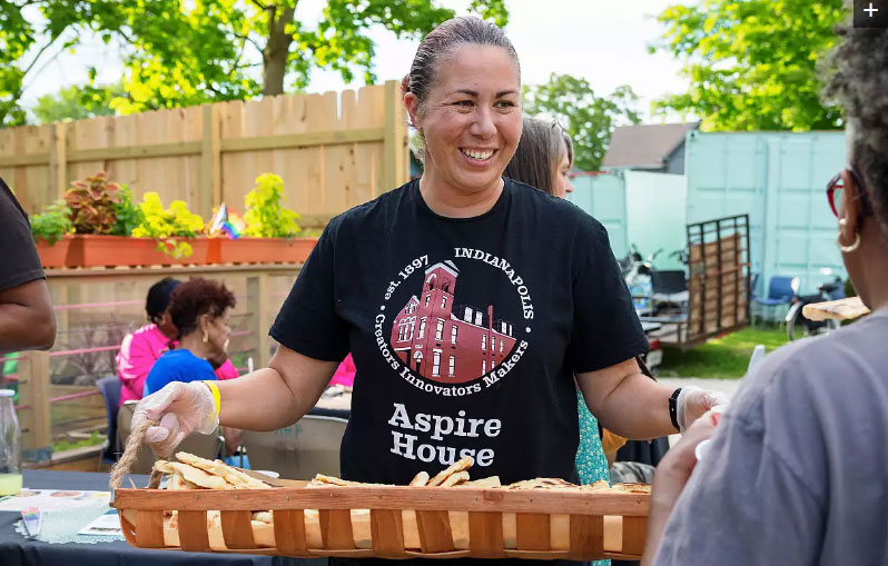 A woman wearing an Aspire House T-shirt holds a basket of bread